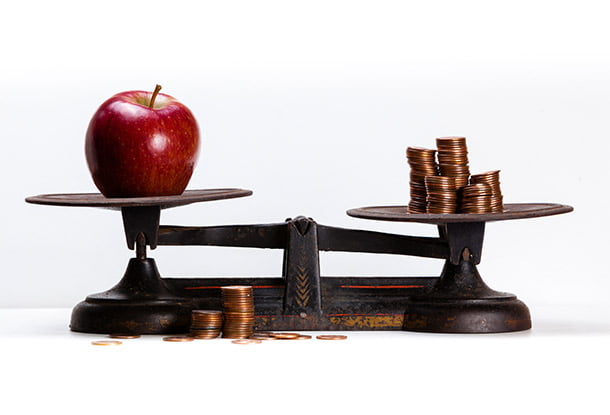 An apple and some coins on opposite sides of a scale (iStockphoto)