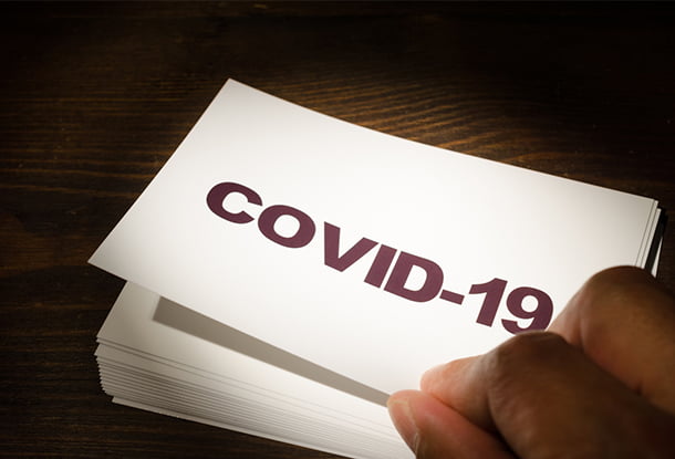 photo: hand picking up card that reads "COVID-19" (iStockphoto)